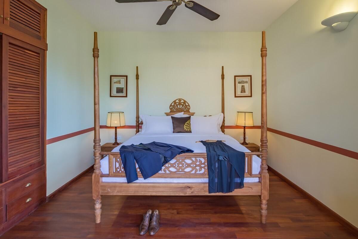 A four-poster bed with a wooden frame, two bedside tables, and a ceiling fan.