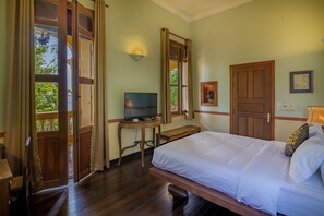 Quarto com cama, escrivaninha e televisão, além de uma porta.