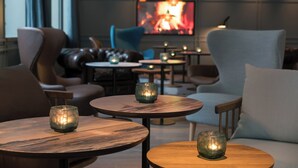 Un espace salon accueillant, avec des tables rondes en bois, des sièges confortables et un éclairage d’ambiance.