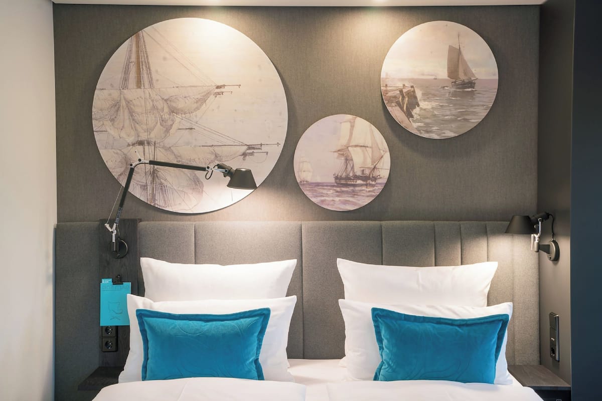 A hotel room with a large bed, two pillows, a headboard, and three circular wall art pieces depicting sailing ships.
