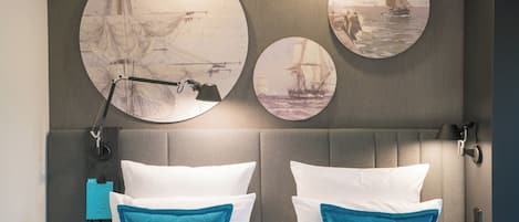 A hotel room with a large bed, two pillows, a nightstand, a lamp, and three circular wall art pieces depicting sailing ships.