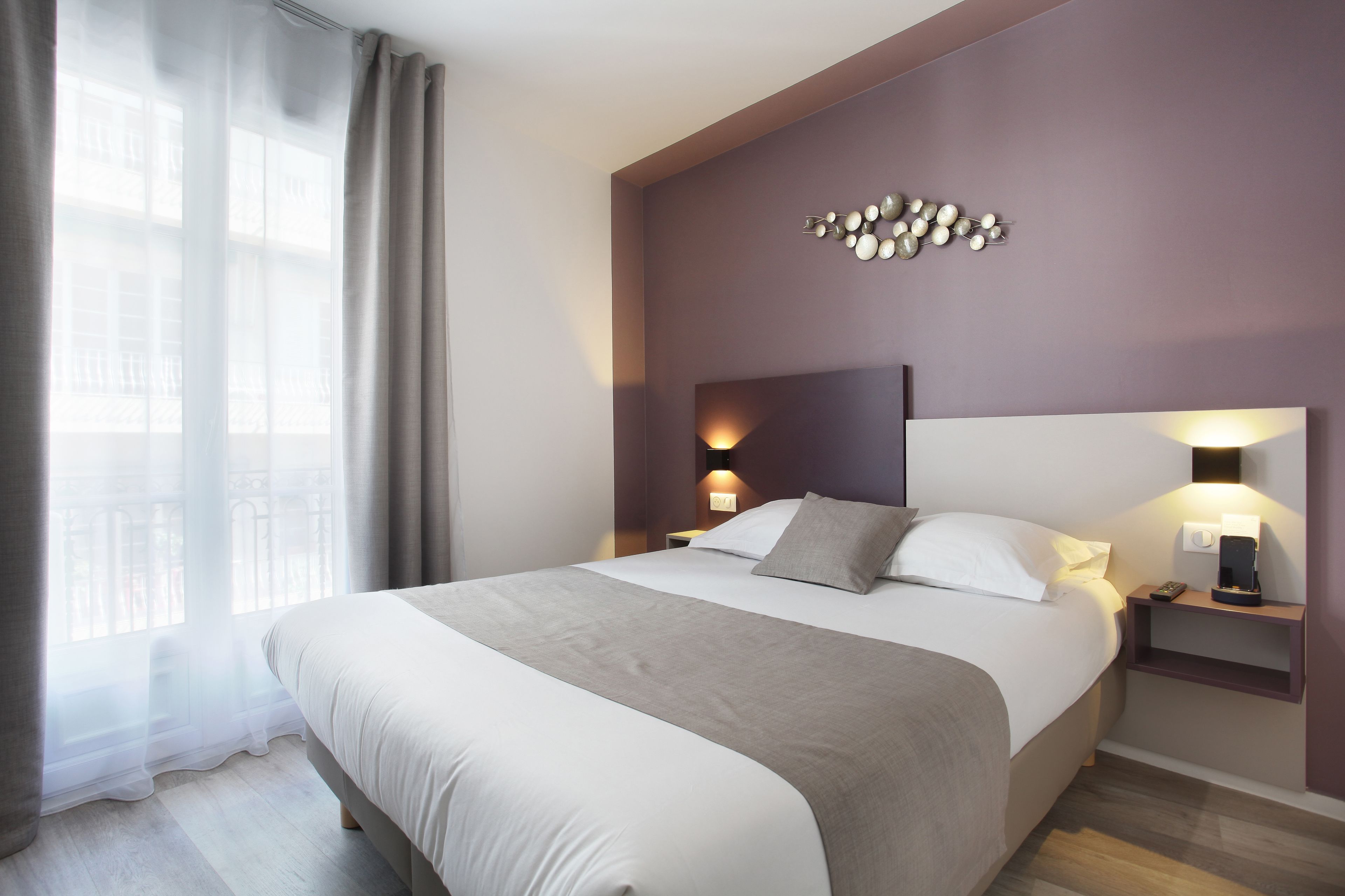 Une chambre d’hôtel moderne avec un grand lit, une table de chevet avec une lampe et un élément décoratif mural.