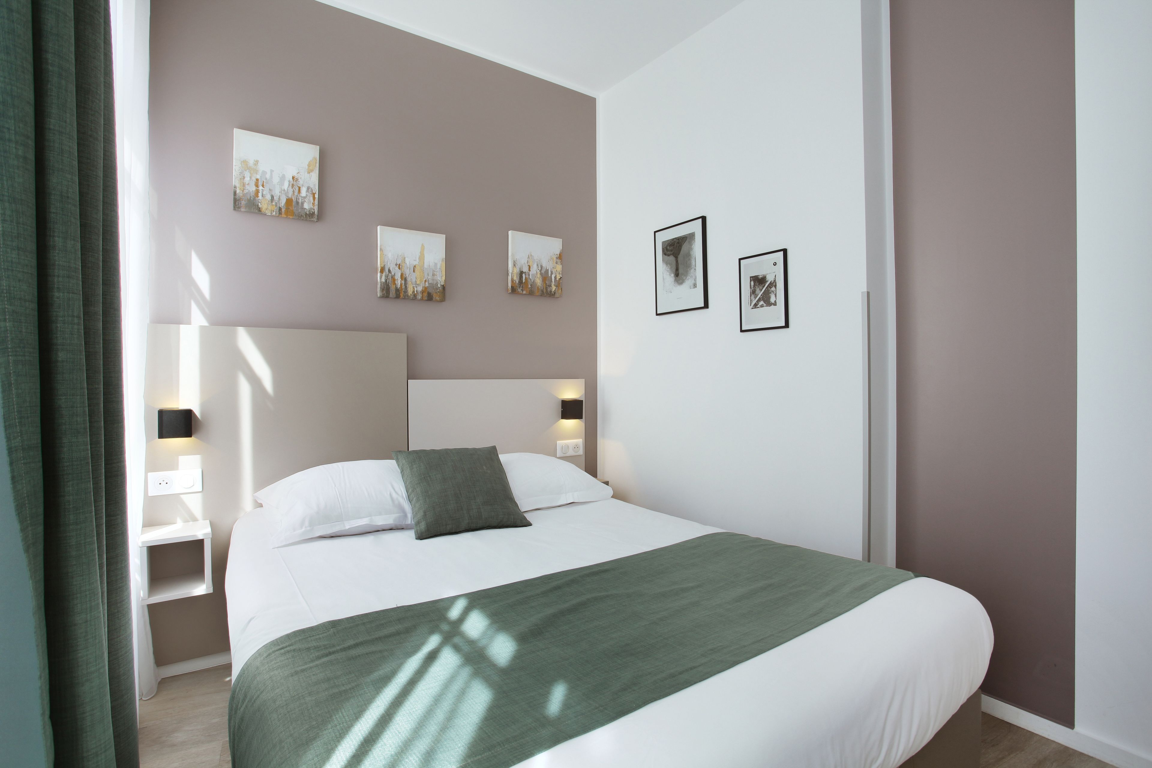 Una habitación de hotel moderna con una cama grande, una mesita de noche, una lámpara de pared y obras de arte en las paredes.