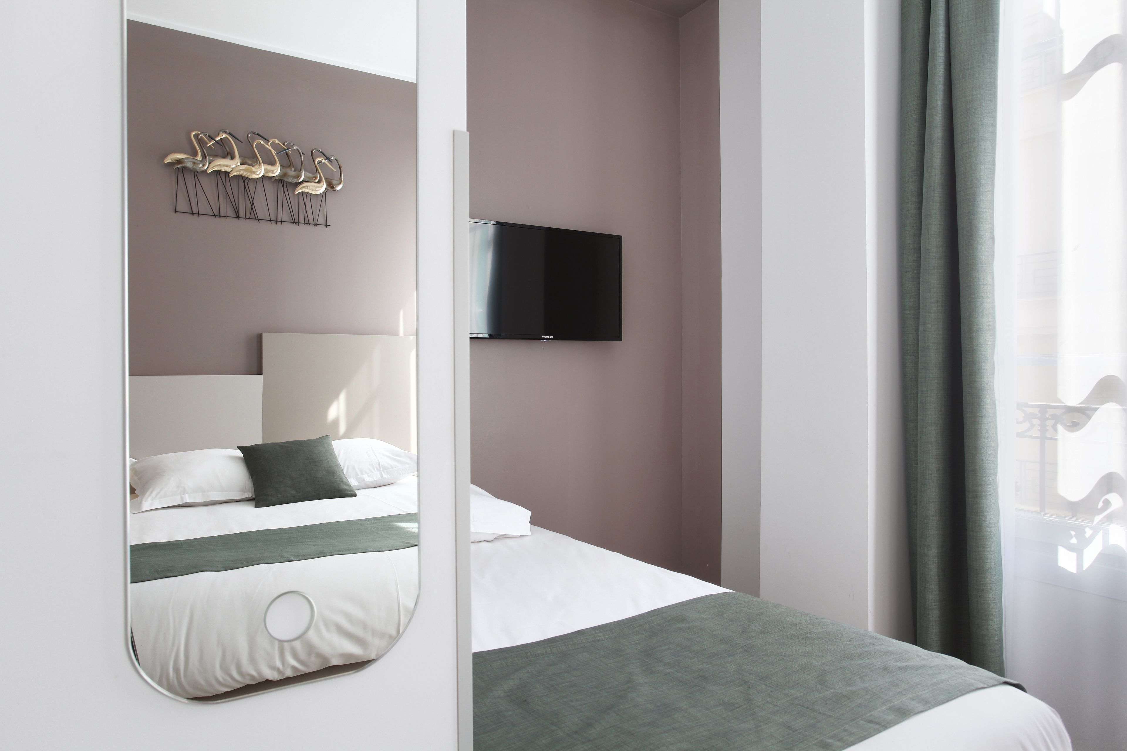 Una habitación de hotel moderna con una cama, un televisor montado, un elemento decorativo en la pared y una ventana con cortinas.