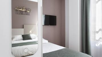 Una habitación de hotel moderna con una cama, un televisor montado, un elemento decorativo en la pared y una ventana con cortinas.