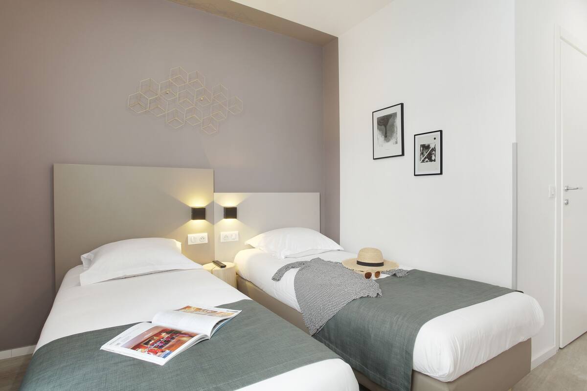 A hotel room with two beds, a wall-mounted light fixture, and a door.