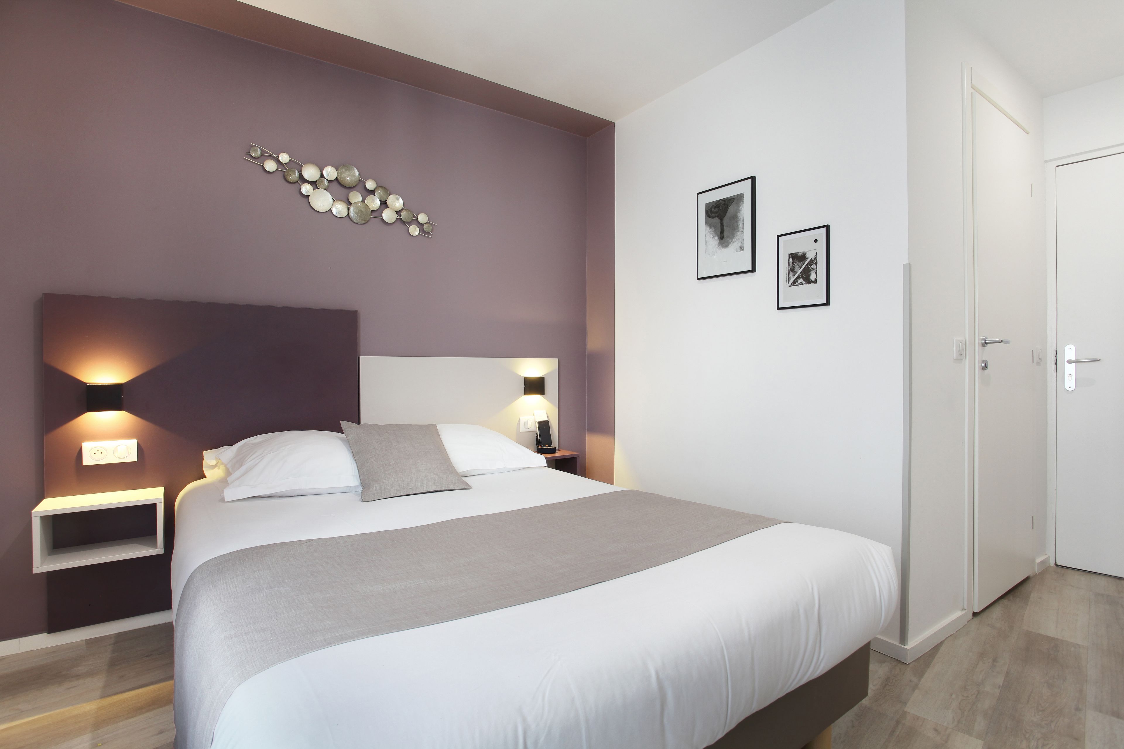 Une chambre moderne avec un grand lit, des lampes de chevet, un luminaire fixé au mur et une porte.