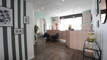 A reception area with a striped wall, a reception desk, two chairs, a coffee table, and a wall-mounted shelf with a vase and a fruit bowl.