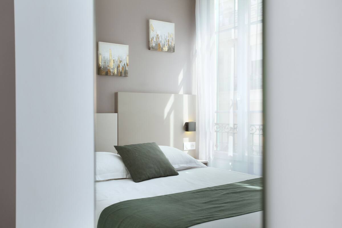 A modern hotel room with a bed, a nightstand, and two wall-mounted artworks.