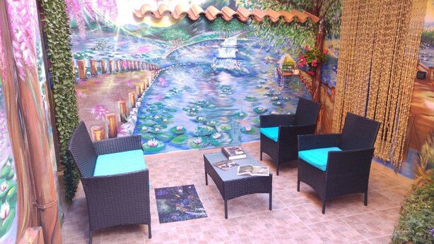 Un patio con mobiliario de mimbre, un mural de una escena fluvial y una planta colgante.