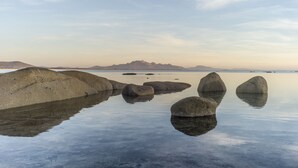 Un lac paisible, avec de gros rochers au premier plan et des montagnes en arrière-plan.