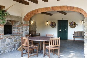 An outdoor patio with a stone wall, wooden table and chairs, a brick oven, and a green door. - Agriturismo Petrognano (Reggello)