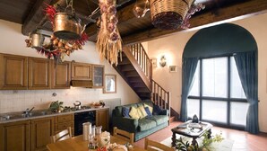 A kitchen with wooden cabinets, a dining table with food items, a staircase, and a large window with curtains. - Agriturismo Petrognano (Reggello)