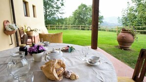 A round table set for tea with a view of a grassy garden and a wooden fence. - Agriturismo Petrognano (Reggello)