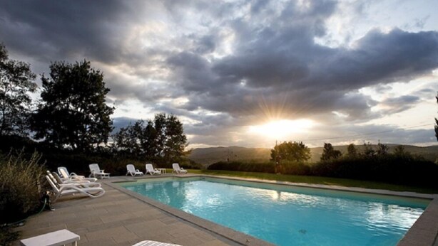 A swimming pool with lounge chairs and a table, surrounded by trees and hills. - Agriturismo Petrognano (Reggello)