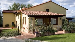 A two-story house with a tiled roof, a covered porch, and a well-maintained garden. - Agriturismo Petrognano (Reggello)