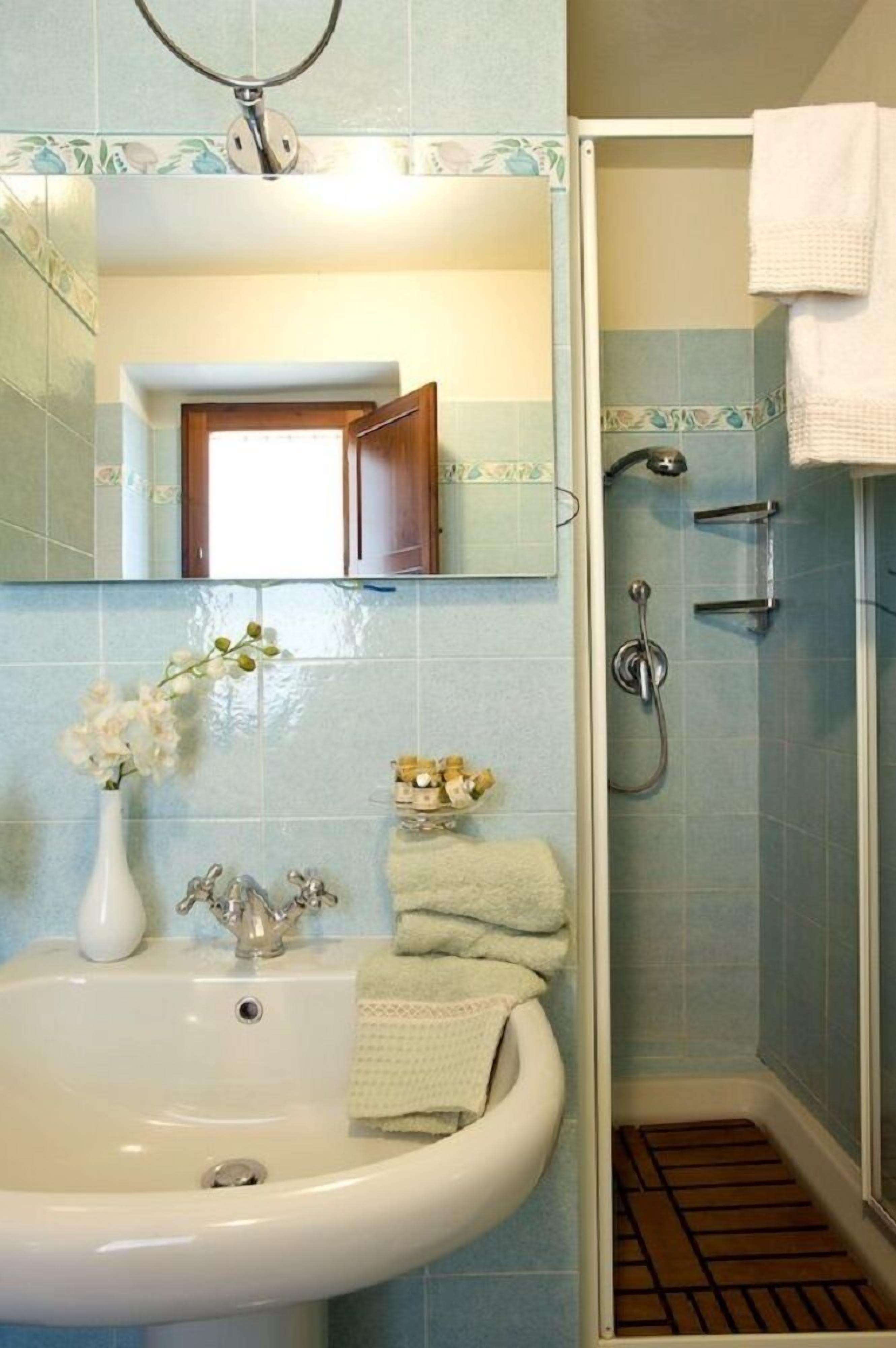 A bathroom with a sink, mirror, shower, and a towel rack.