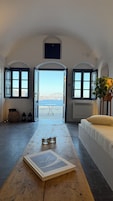 Una habitación con vistas al mar, una mesa de madera con un libro y una cama con un almohadón.