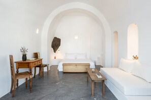 Een minimalistische slaapkamer met een bed, een houten bureau, een stoel, een bank en een bijzettafeltje.