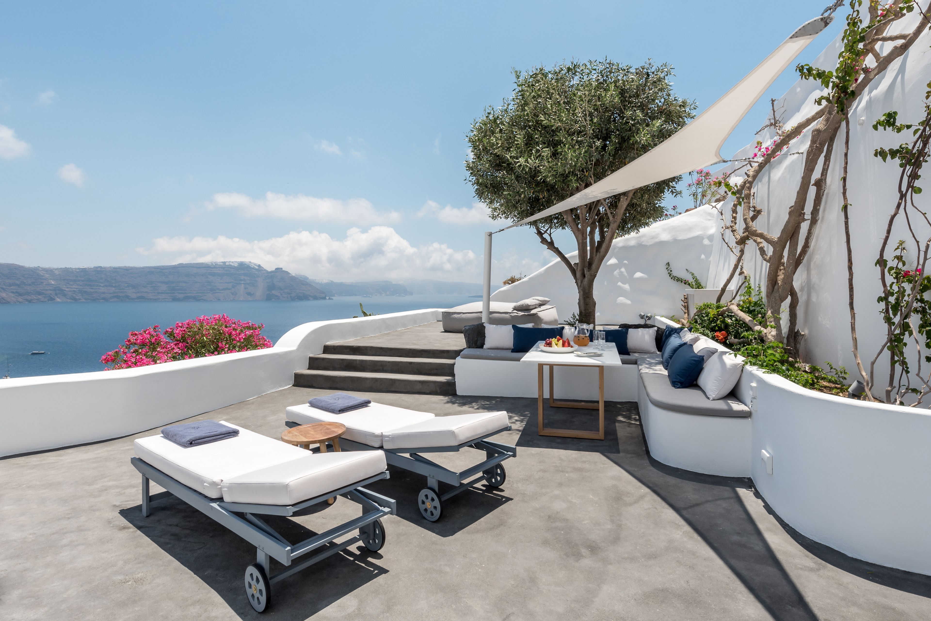 A modern outdoor lounge area with a view of the sea, featuring a sofa set, a lounge chair, and a small table.