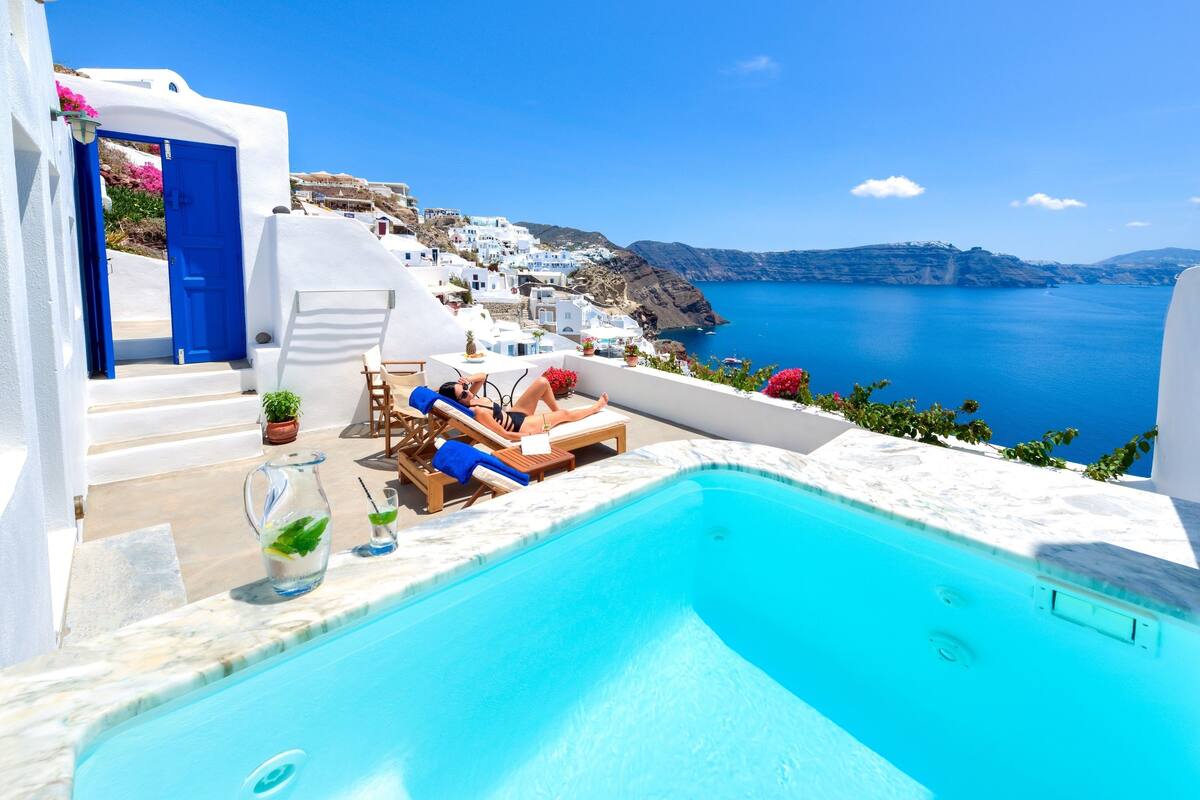 Zona de piscina con sillones de descanso y vistas al mar y edificios blancos.