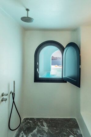 Een badkamer met een douche, een raam met uitzicht op zee, en een marmeren vloer.