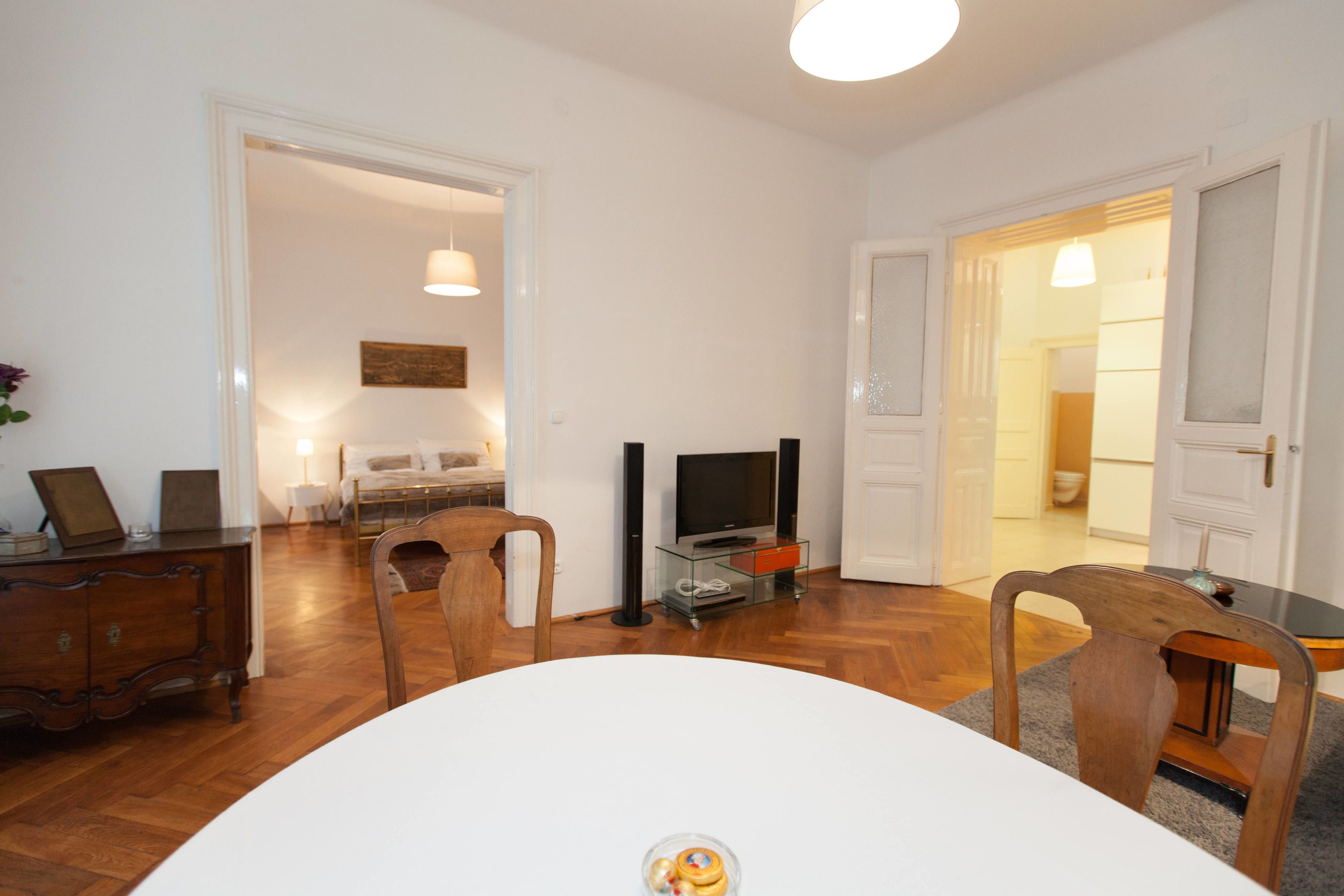 A modern living room with a round dining table, wooden chairs, a TV stand, and a sofa.