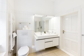A modern bathroom with a toilet, sink, and shower. It features white fixtures and a large mirror.
