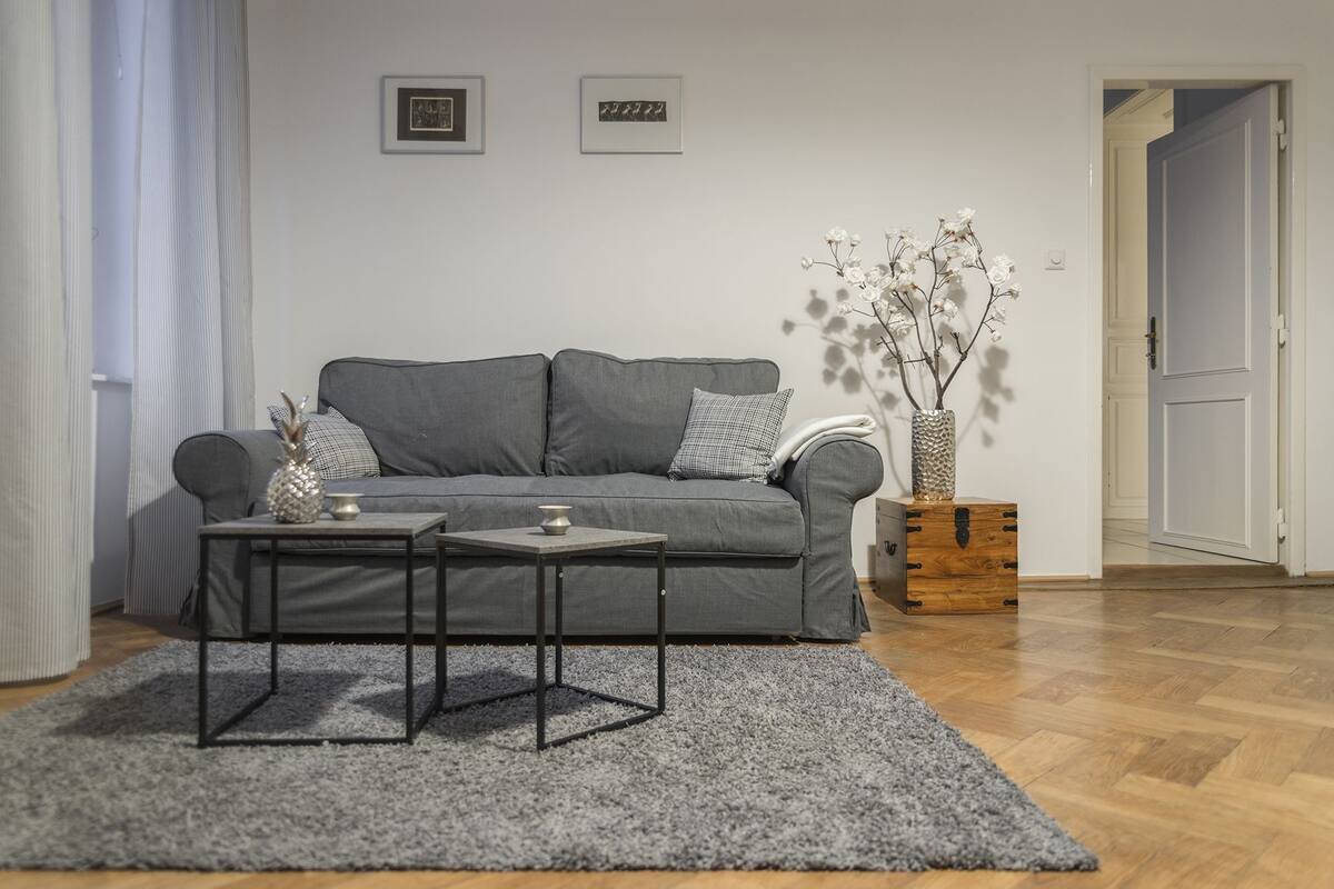 A modern living room with a grey sofa, two side tables, a grey rug, and a wooden chest of drawers.