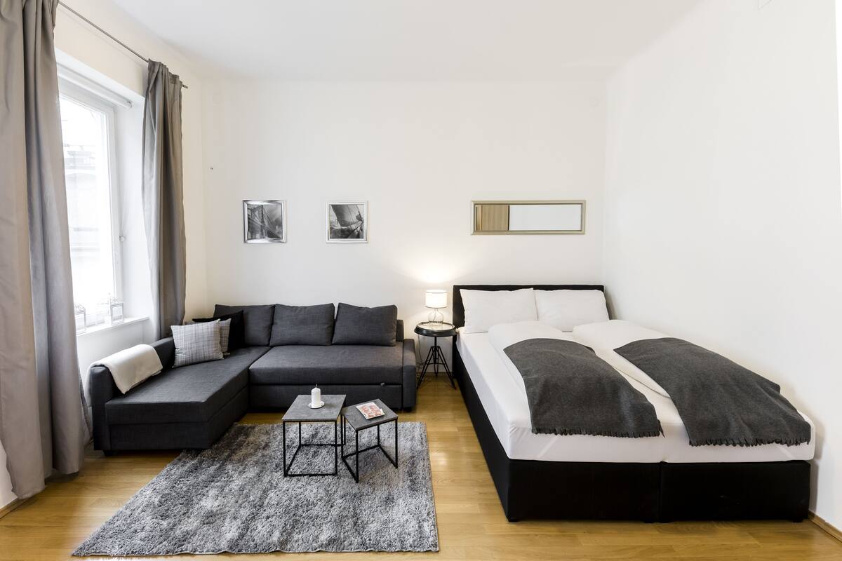 A modern bedroom with a black and white bed, a grey sofa, a small table with a candle, and two framed pictures on the wall.