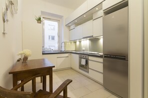 A modern kitchen with stainless steel appliances, a wooden dining table, and a small window with a view of the outside.