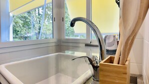 A modern kitchen with a large sink, wooden utensils holder, and large windows with yellow blinds. - Giulio Cesare Luxury Apartment (Rome)