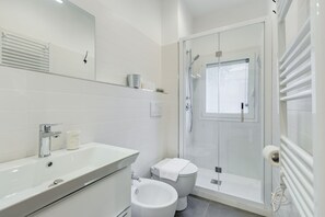 Un baño moderno con lavamanos blanco, inodoro y ducha con mampara de vidrio.