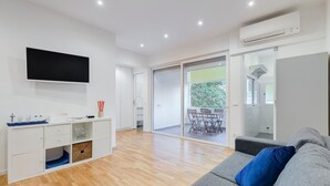 A modern living room with a grey sofa, a flat-screen TV mounted on the wall, a wooden floor, and a sliding glass door leading to an outdoor area with a table and chairs. - Giulio Cesare Luxury Apartment (Rome)