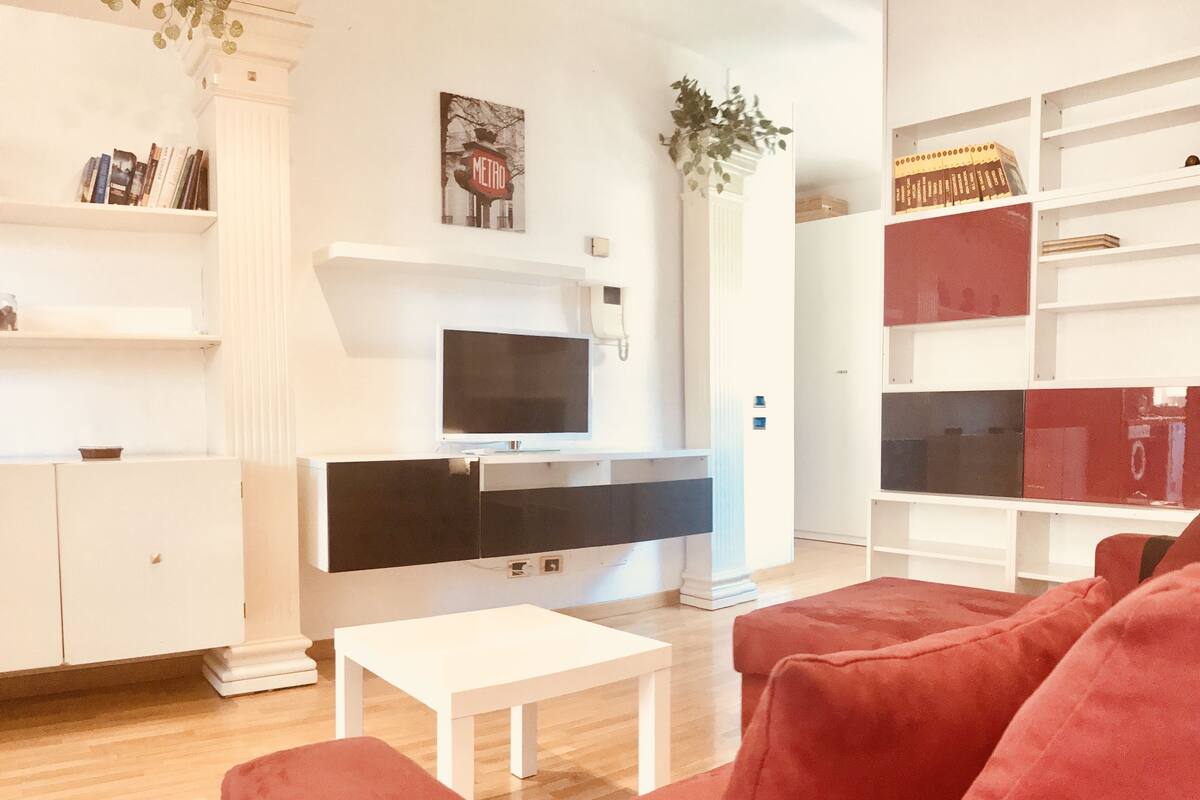 A modern living room with a flat-screen TV, a white coffee table, and red sofas.