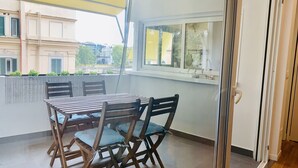 A balcony with a table and chairs, a yellow awning, and a view of buildings and trees. - Giulio Cesare Luxury Apartment (Rome)
