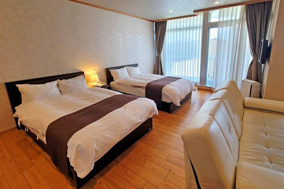 A hotel room with two beds, a sofa, and a TV.