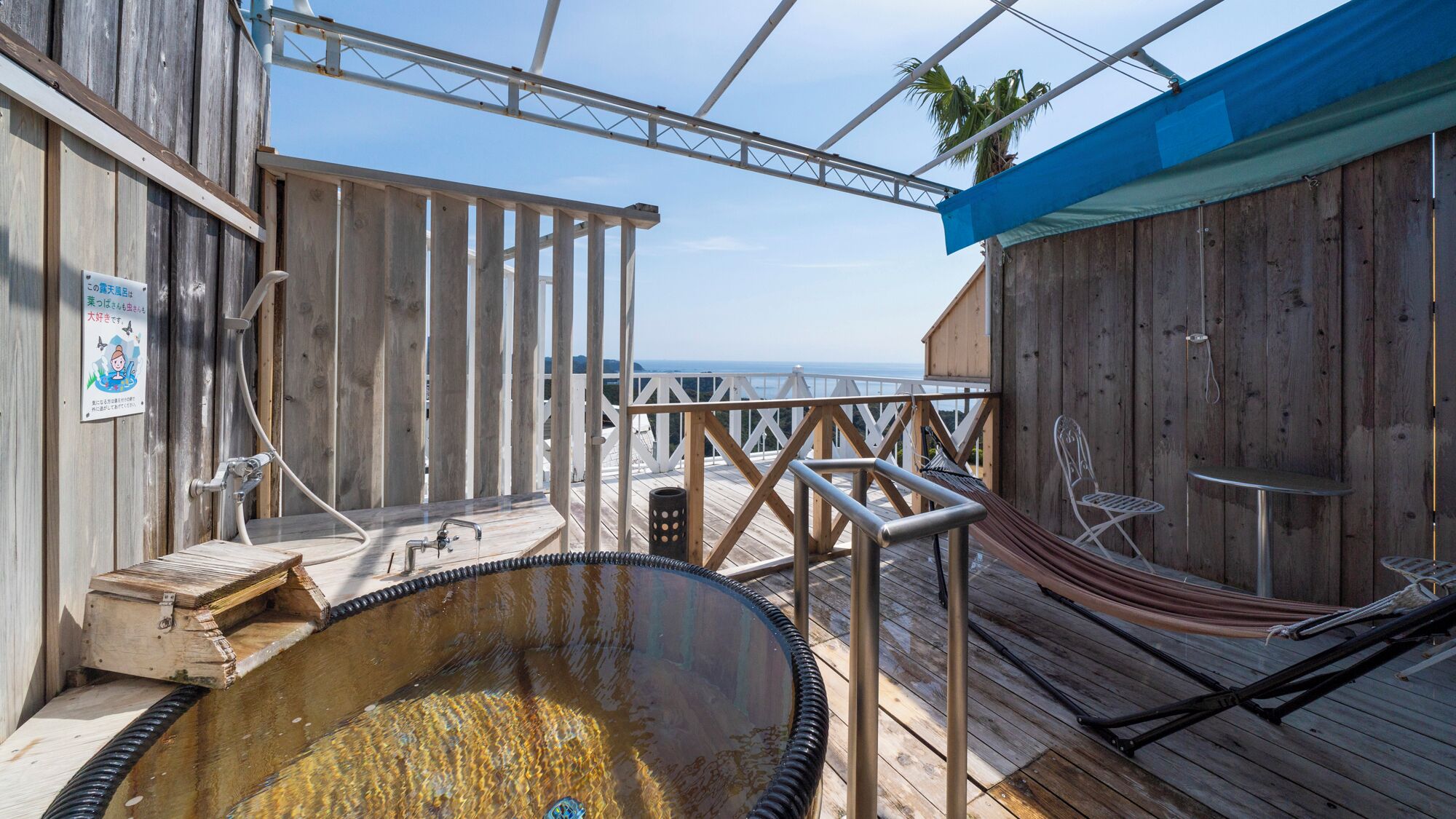 A wooden deck with a hot tub, a hammock, and a view of the ocean.