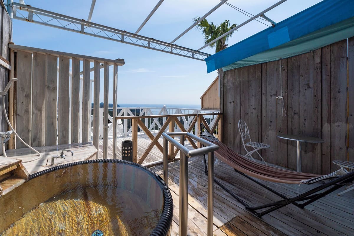 A wooden deck with a hot tub, a hammock, and a view of the ocean.