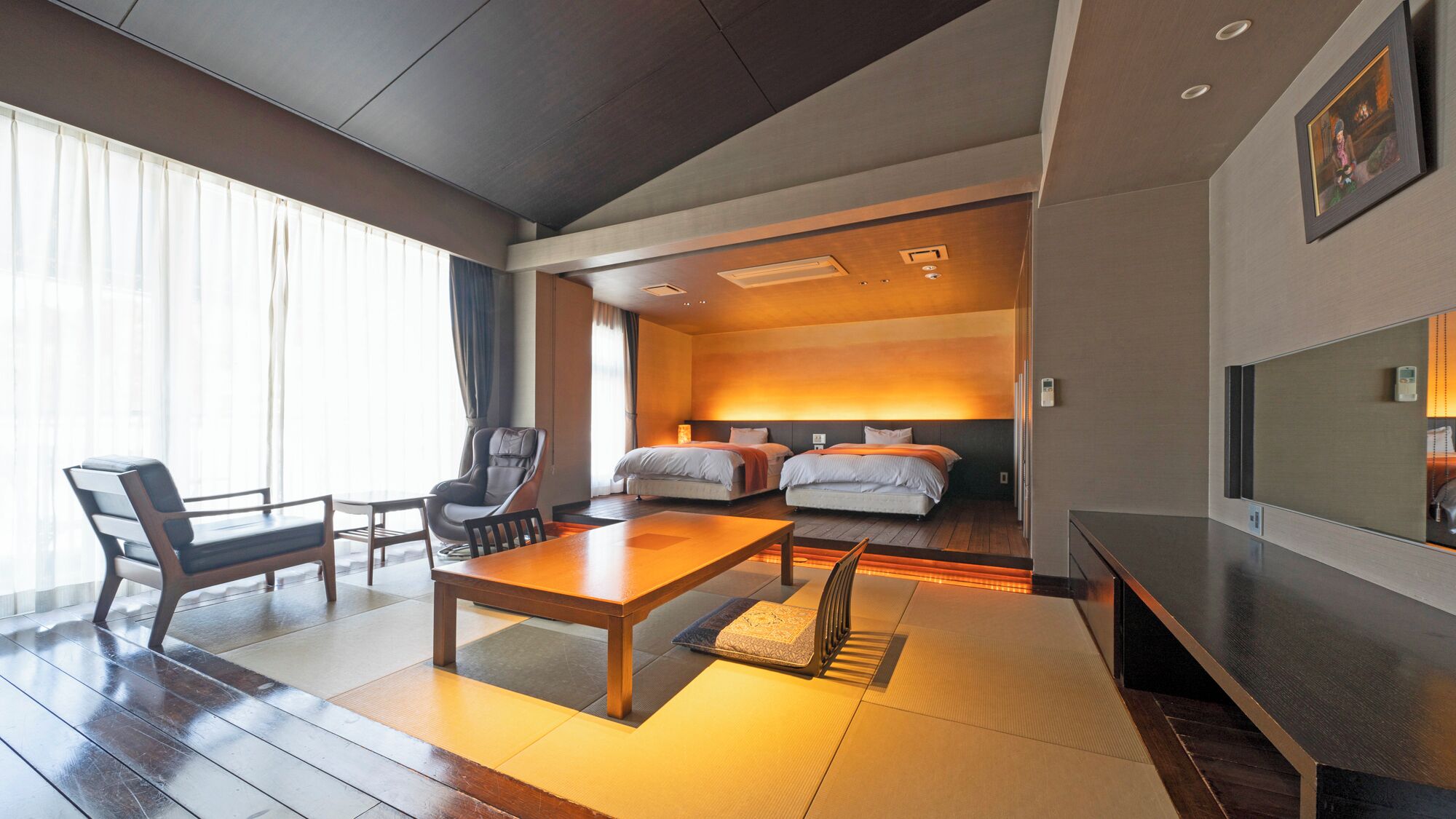 Une chambre d’hôtel avec un plancher en bois, une table à manger, deux lits, un canapé et un téléviseur.