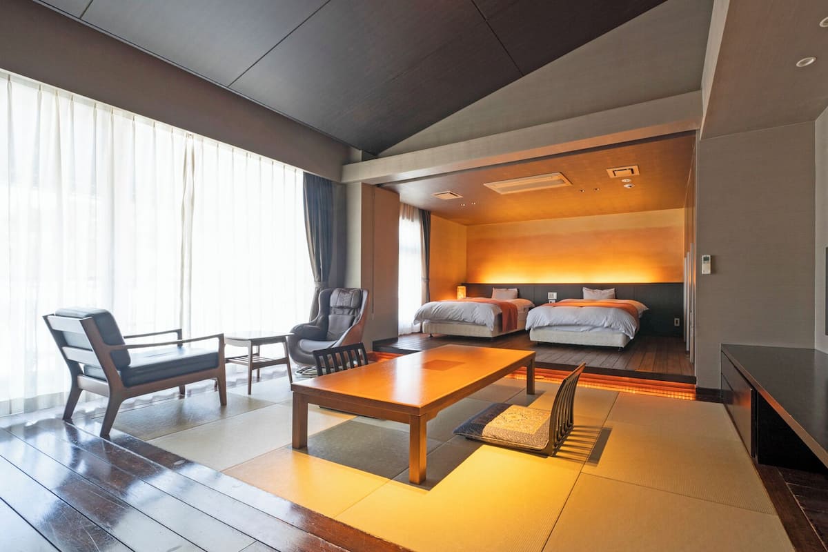 A hotel room with a wooden floor, a dining table, two beds, a sofa, and a TV.