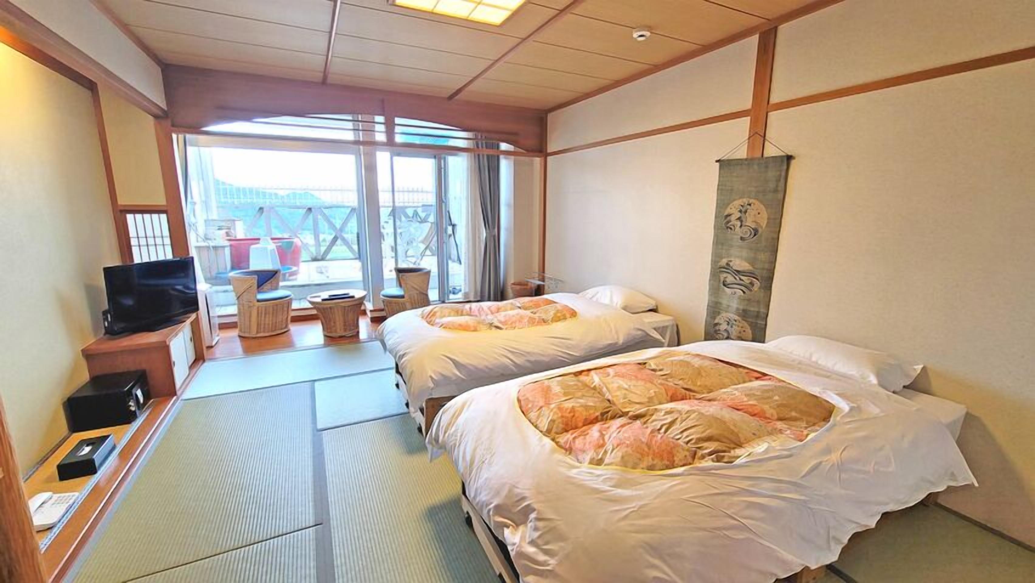 A hotel room with two beds, a TV, a desk with a phone, and a view of the outside.