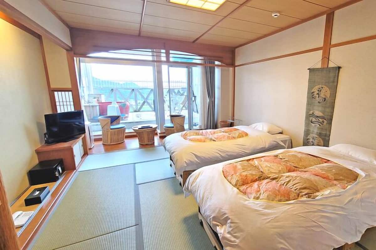 A hotel room with two beds, a TV, a desk with a phone, and a view of the outside.