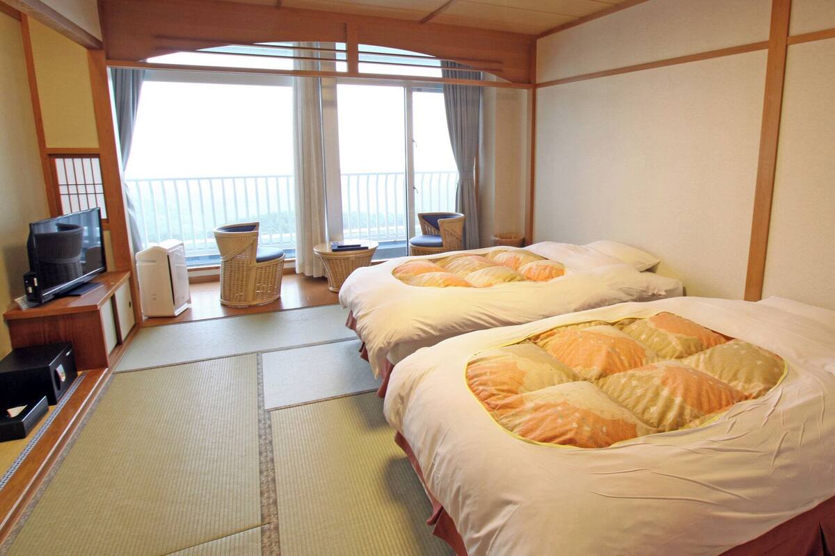 A hotel room with two beds, a television, a small table, and a view of the outside.