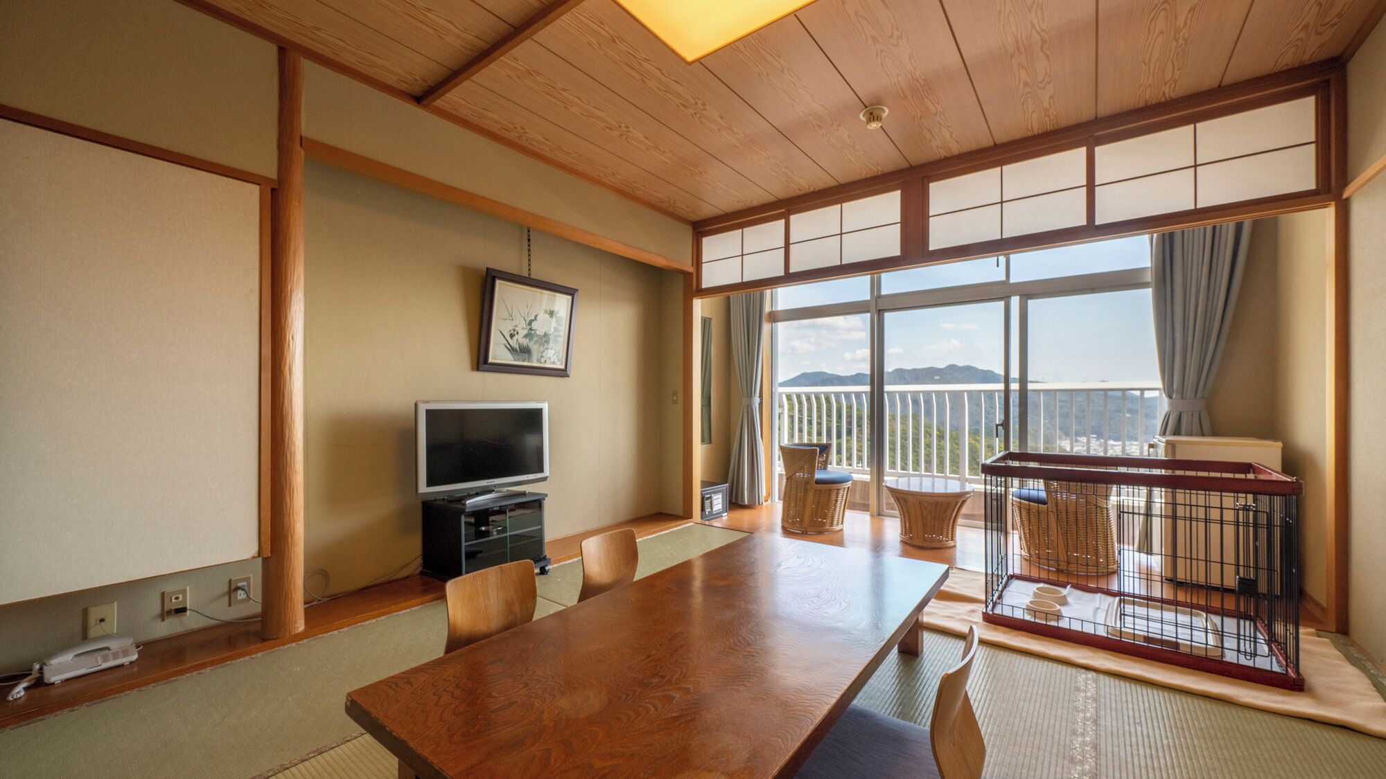 Une pièce de style japonais traditionnel, avec un sol recouvert de tatamis, une table en bois, un téléviseur et un balcon offrant une vue dégagée.
