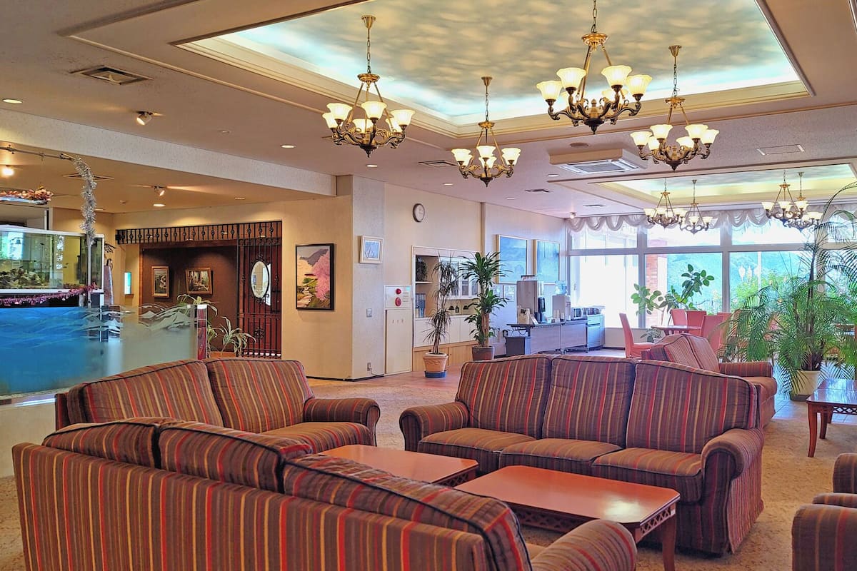 A hotel lobby with striped sofas, chandeliers, a pool area, and large windows.