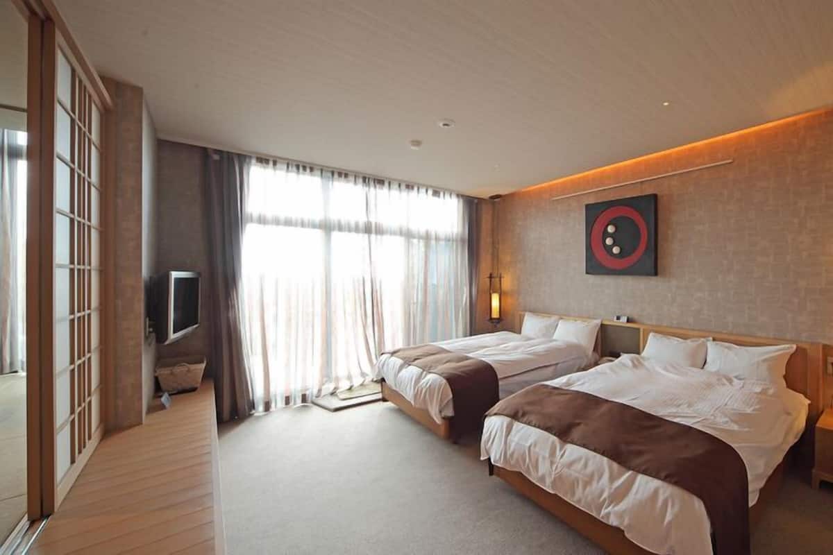 A hotel room with two beds, a TV, a wall-mounted artwork, and a bedside table with a lamp.