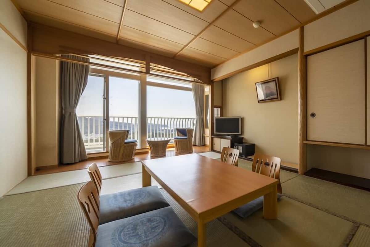 A traditional Japanese-style room with tatami flooring, a low wooden table, and a television on a cabinet.