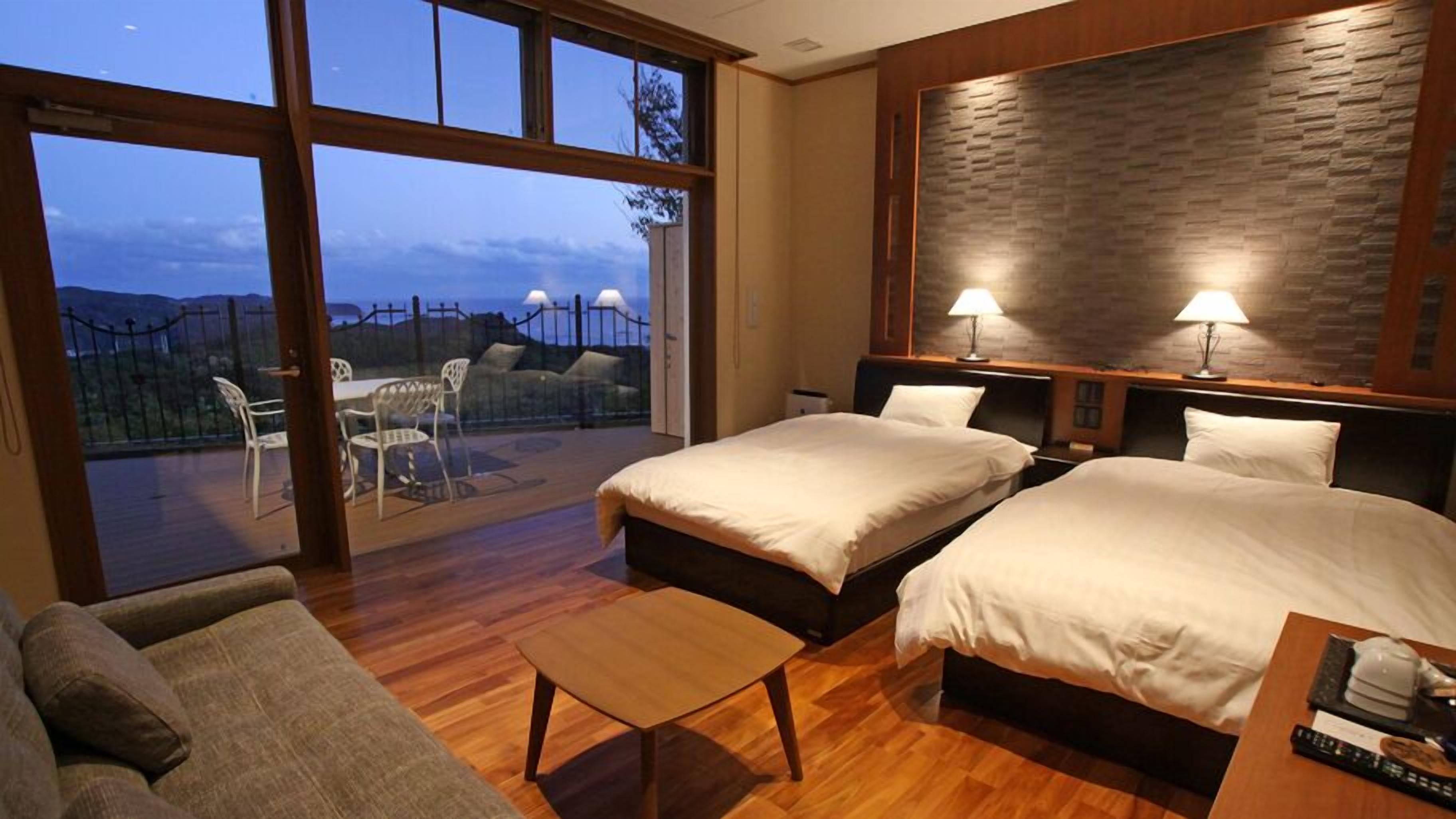 A hotel room with two beds, a sofa, a small table, and a balcony with chairs.