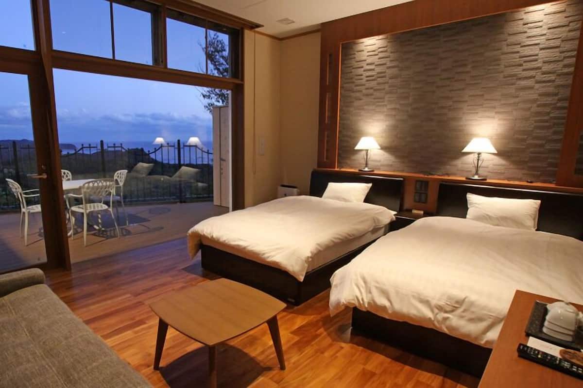A hotel room with two beds, a sofa, a small table, and a balcony with chairs.